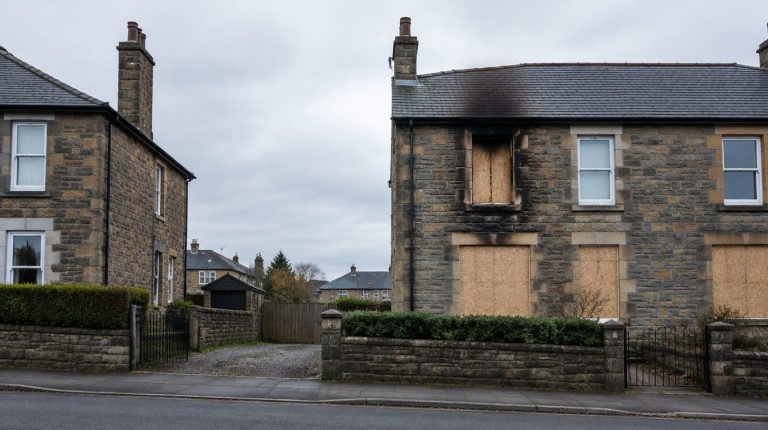 Fire damaged stone semi-detached house in Scotland with boarded up windows and smoke staining