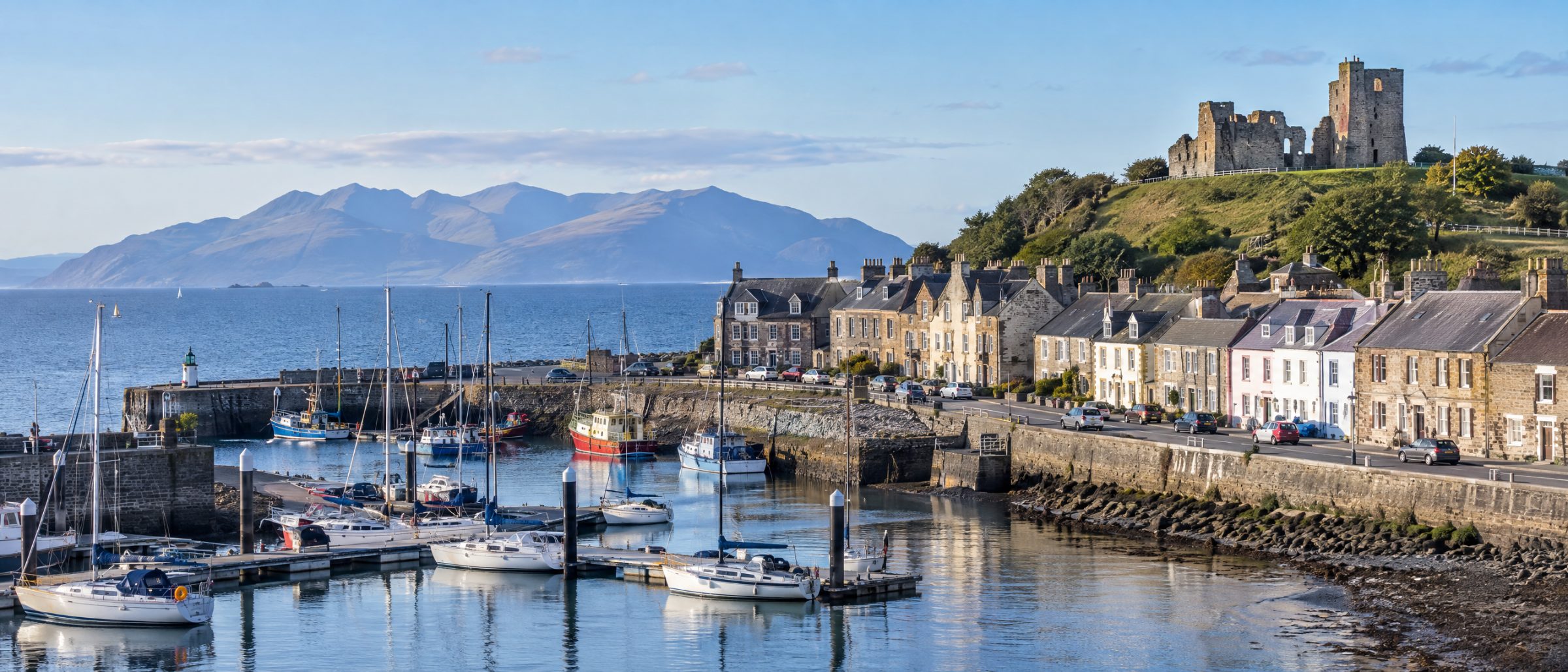 Ardrossan harbour with stone houses, moored boats and the castle ruins on the hill